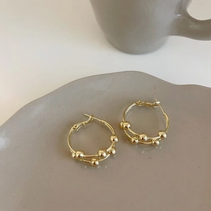 Detailed view of double-layer gold hoop earrings with small beads on a ceramic tray