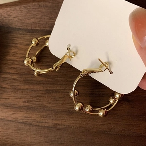 Double-layered 18K gold circle earrings with small golden beads on wood background