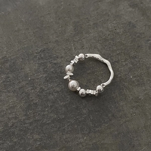 Elegant beaded ring featuring white pearls and textured silver pieces on stone surface
