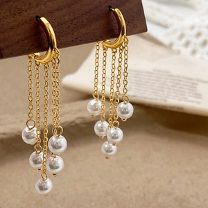 Macro detail of gold chain tassel earrings with white pearls on a dark wood block
