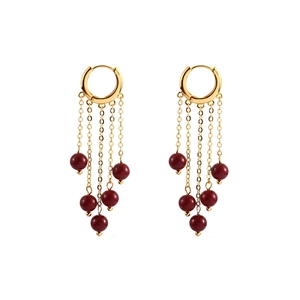 Macro shot of gold chain tassel earrings with deep red spherical beads on white background