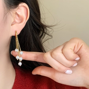 Elegant gold chain fringe earrings with white pearls shown in a side-view close-up shot