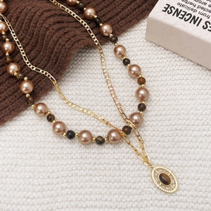 Gold double-layer necklace with tiger eye stone pendant and pearls on knit fabric