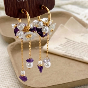 Macro shot of elegant gold hoop earrings with purple gems, pearls and floral tassels