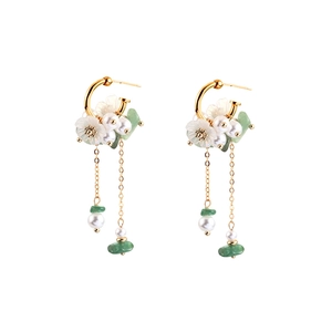 Detail of floral drop earrings featuring white petals, green stones and gold chains