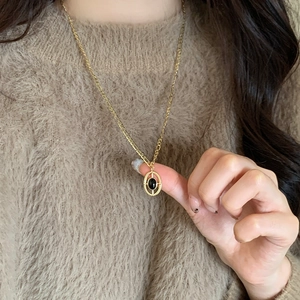 Collier long doré avec pendentif oeil de tigre porté sur un pull en maille marron