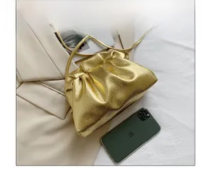 Detail view of gold metallic cloud bucket bag with phone for size comparison