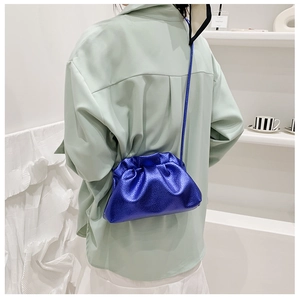 Detail of metallic blue cloud bag with pleated texture on model wearing green shirt