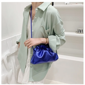 Detail of metallic blue pleated dumpling bag with adjustable shoulder strap on model