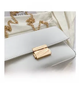 Close-up of minimalist white faux leather bag with elegant gold rectangle push-lock and chain