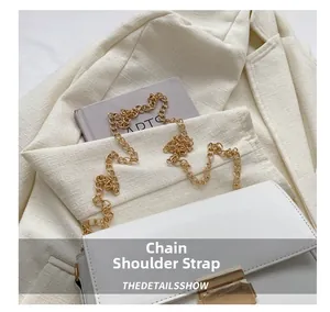 Detail shot of the golden chain shoulder strap and metallic buckle on a white leather bag