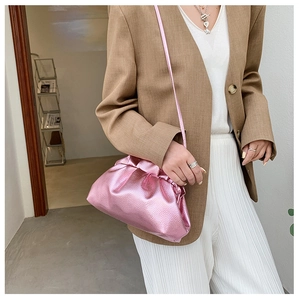 Metallic pink drawstring bucket bag with pleated texture worn on model over tan blazer