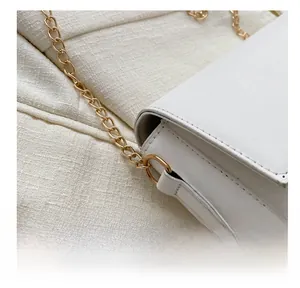 Detail of the golden metal chain connected to the white faux leather bag via D-ring