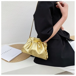 Detail of a metallic gold pleated dumpling bag with a fine chain strap on a black blazer