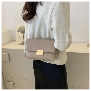 Detail of minimalist beige rectangle shoulder bag with gold metal chain and square lock