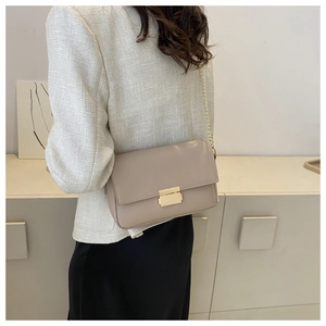 Detail of light beige crossbody bag with gold square buckle on a model wearing tweed