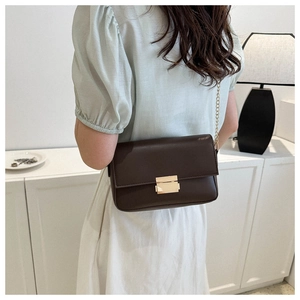 Detail view of dark brown leather chain bag with elegant gold metal buckle on female model