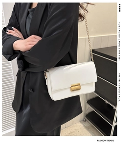 Detailed view of white leather crossbody bag with gold buckle and chain strap shown on model