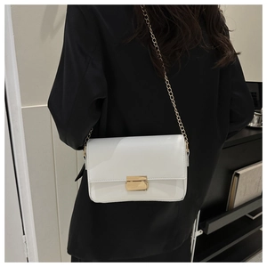 Detailed view of white rectangular crossbody bag with golden chain strap on black blazer