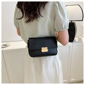 Detail showing the gold chain strap and metallic lock on a black minimalist shoulder bag