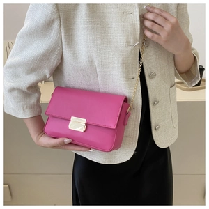 Close-up of bright pink leather crossbody bag with gold chain strap and square buckle