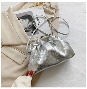 Detailed view of silver metallic cloud bag with soft pleats on a stylish beige blazer