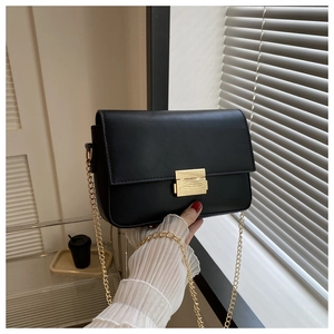 Detail of black leather square bag showing the golden metal buckle and chain strap