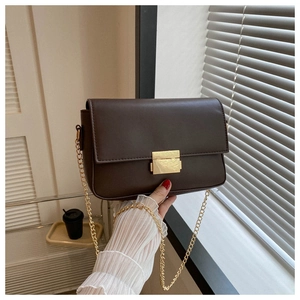 Detail of dark brown leather handbag featuring a golden rectangular lock and chain strap