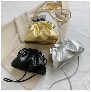 Three metallic colors of pleated drawstring bucket bags displayed on a textured fabric