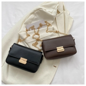 Detail of minimalist black and brown flap bags with gold chain straps on white blazer
