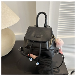 Close-up of black PU leather backpack with FAUTOR logo and pink plush ball charm