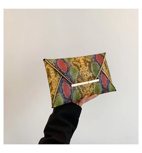 Macro detail of multi-color snakeskin texture and gold metal trim on envelope clutch bag