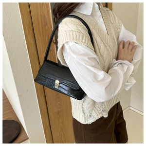 Dettaglio borsa a spalla nera effetto coccodrillo indossata da una modella su un gilet