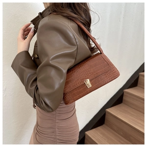 Brown crocodile pattern baguette bag with gold buckle worn on the shoulder by model