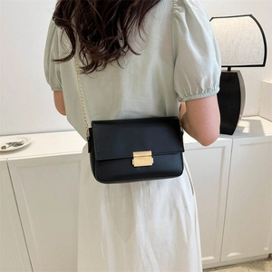 Minimalist black leather crossbody bag with gold chain strap shown on model shoulder