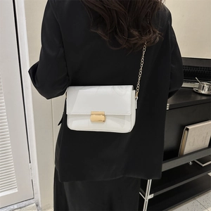 Minimalist white leather crossbody bag with gold chain strap shown on a model