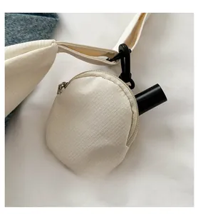 Detail of a beige canvas mini pouch with black carabiner attached to a wide shoulder strap