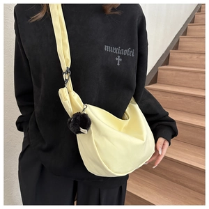 Detail of light yellow crescent crossbody bag with nylon texture and black plush ball