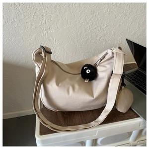 Detail of beige crescent crossbody bag with ribbed fabric texture and plush charm