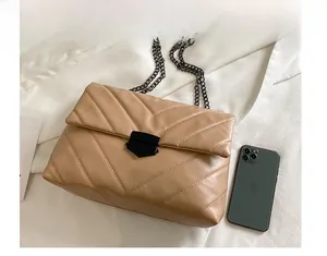 Close-up of beige quilted bag with black metal chain strap and twist-lock clasp detail