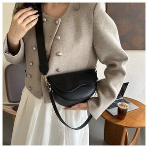 Photo lifestyle d'un sac besace en cuir noir avec large bandoulière sur une table en bois