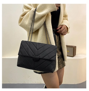 Detail of black chevron quilted shoulder bag with dark metal chain strap and sleek buckle