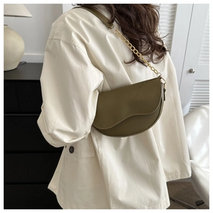 Détail d'un sac selle vert olive avec chaîne dorée porté à l'épaule par un mannequin