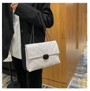 Close-up of a white quilted shoulder bag with V-pattern stitching and dark metal chain