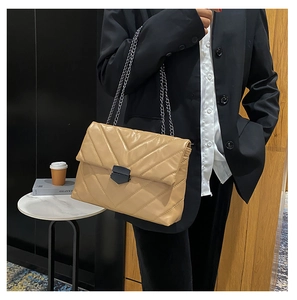 Detail of khaki quilted shoulder bag with black V-clasp and silver chain on model