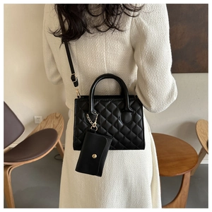Détail d'un sac bandoulière matelassé noir avec boucle dorée et mini porte-monnaie charm