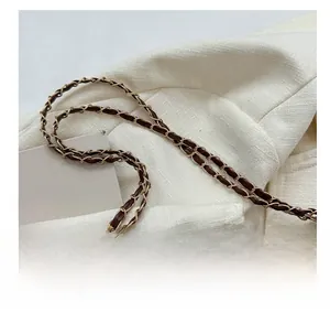 Detail of dark brown quilted bag with leather woven chain strap on white blazer