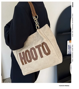 Detail of canvas tote bag featuring brown leather trim and golden metal chain strap