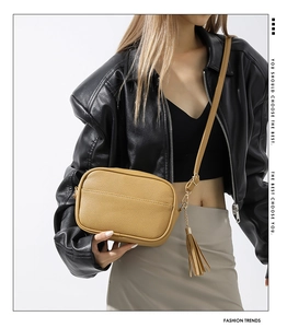 Detail of mustard yellow textured leather crossbody bag with long tassel and gold hardware