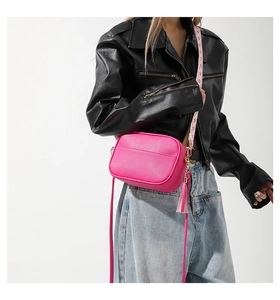Detail of rose red crossbody camera bag with woven strap and gold zipper on leather texture